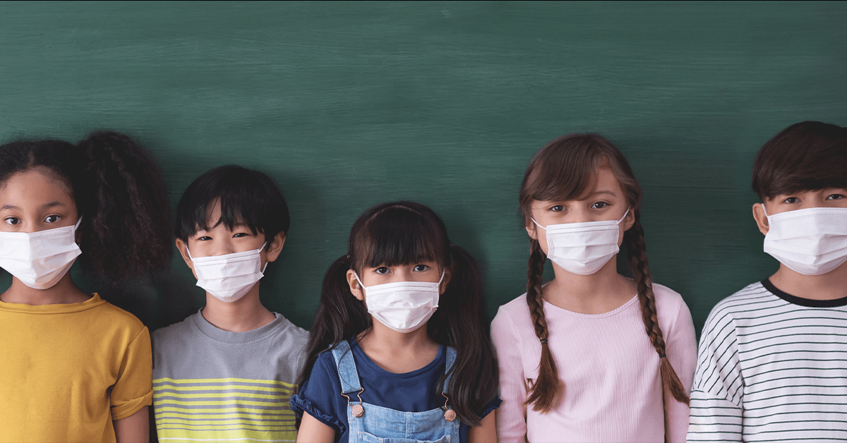 students wearing masks standing in front of blackboard